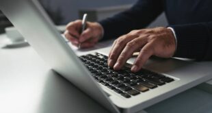 Advogado digita em computador com uma mão e escreve com outra