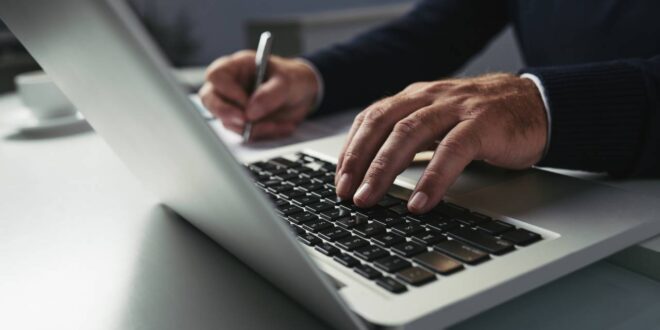 Advogado digita em computador com uma mão e escreve com outra